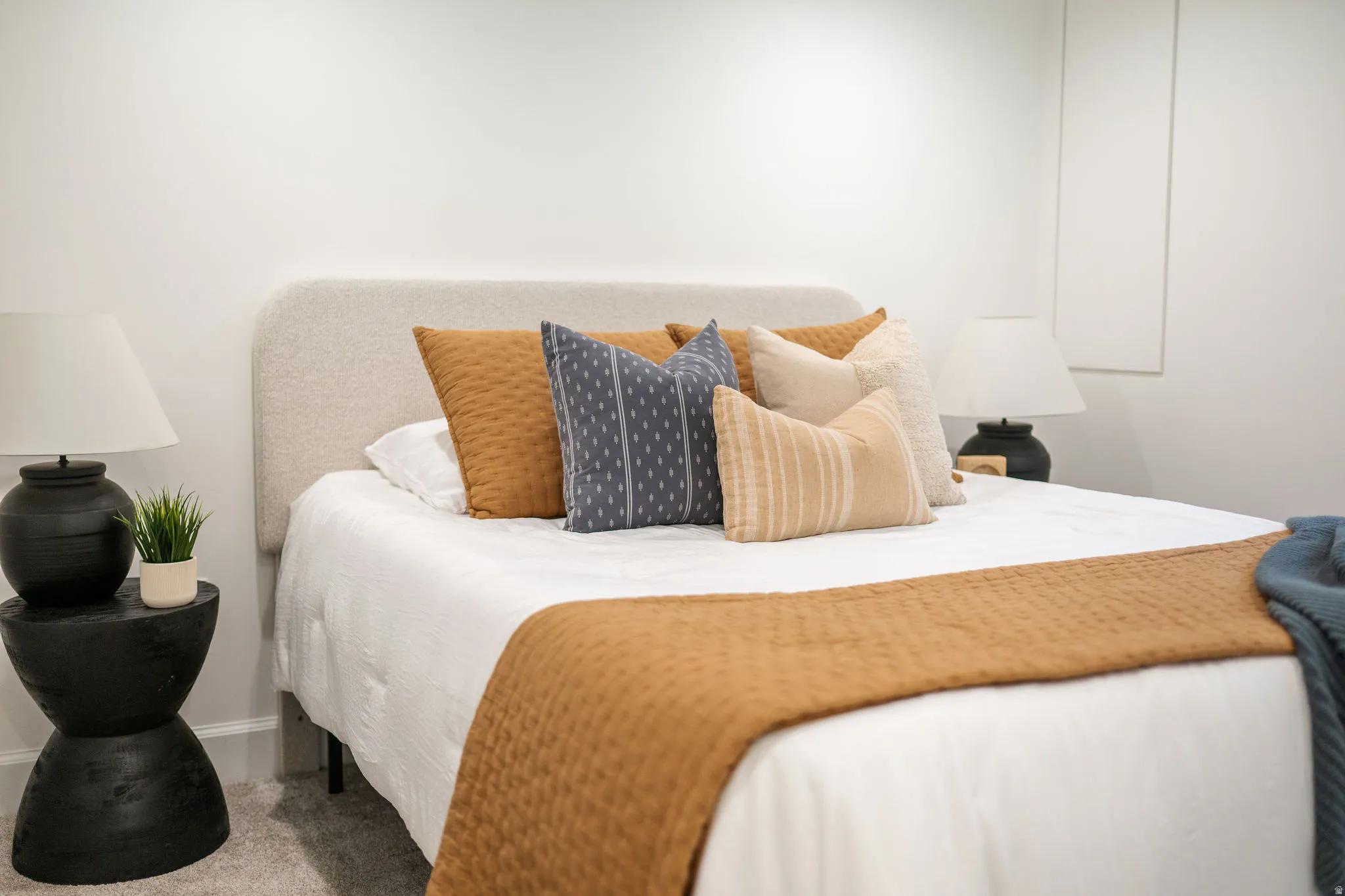 Bedroom featuring a light-toned upholstered headboard, clean white walls, and soft grey carpeting