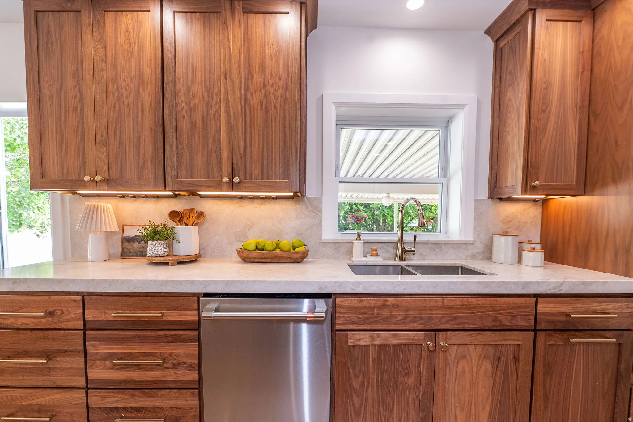 Kitchen featuring custom wood cabinetry with undermount lighting, white countertop, stone backsplash, and stainless steel undermount double sink with a single-handle faucet
