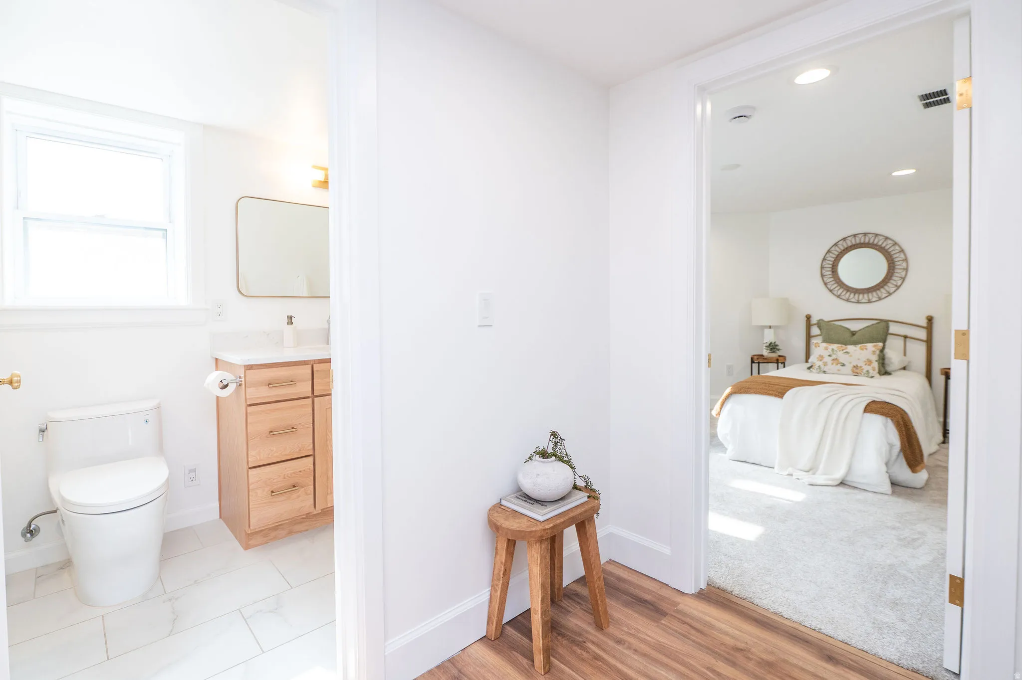 Hardwood-style flooring extends through the hallway, opening to a bedroom with recessed lighting and a bathroom featuring a window, tiled flooring, and a wood-finish vanity with a countertop