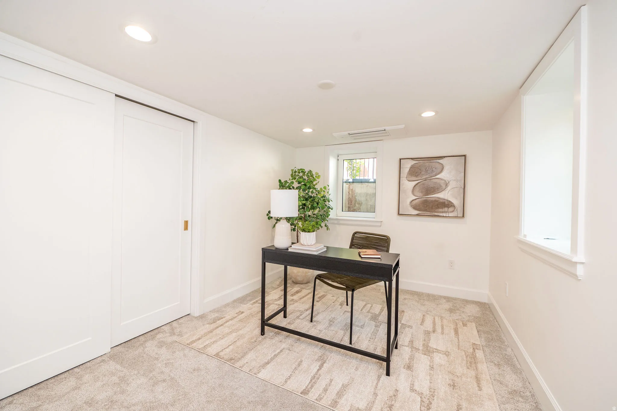 Recessed lighting illuminates this room, featuring light-colored carpeting, a window with a deep sill, and a white sliding panel door
