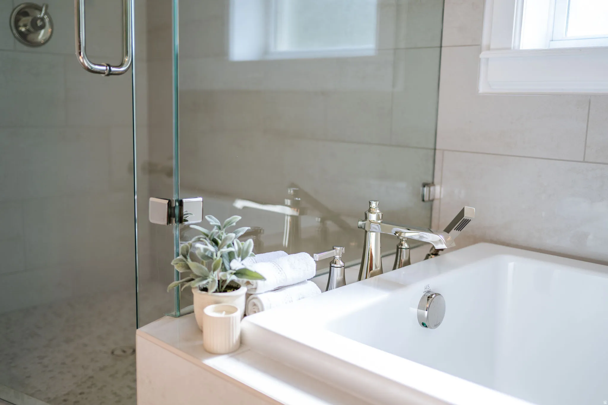 Bathtub featuring deck-mounted chrome faucet, integrated shower wand, and white tile surround