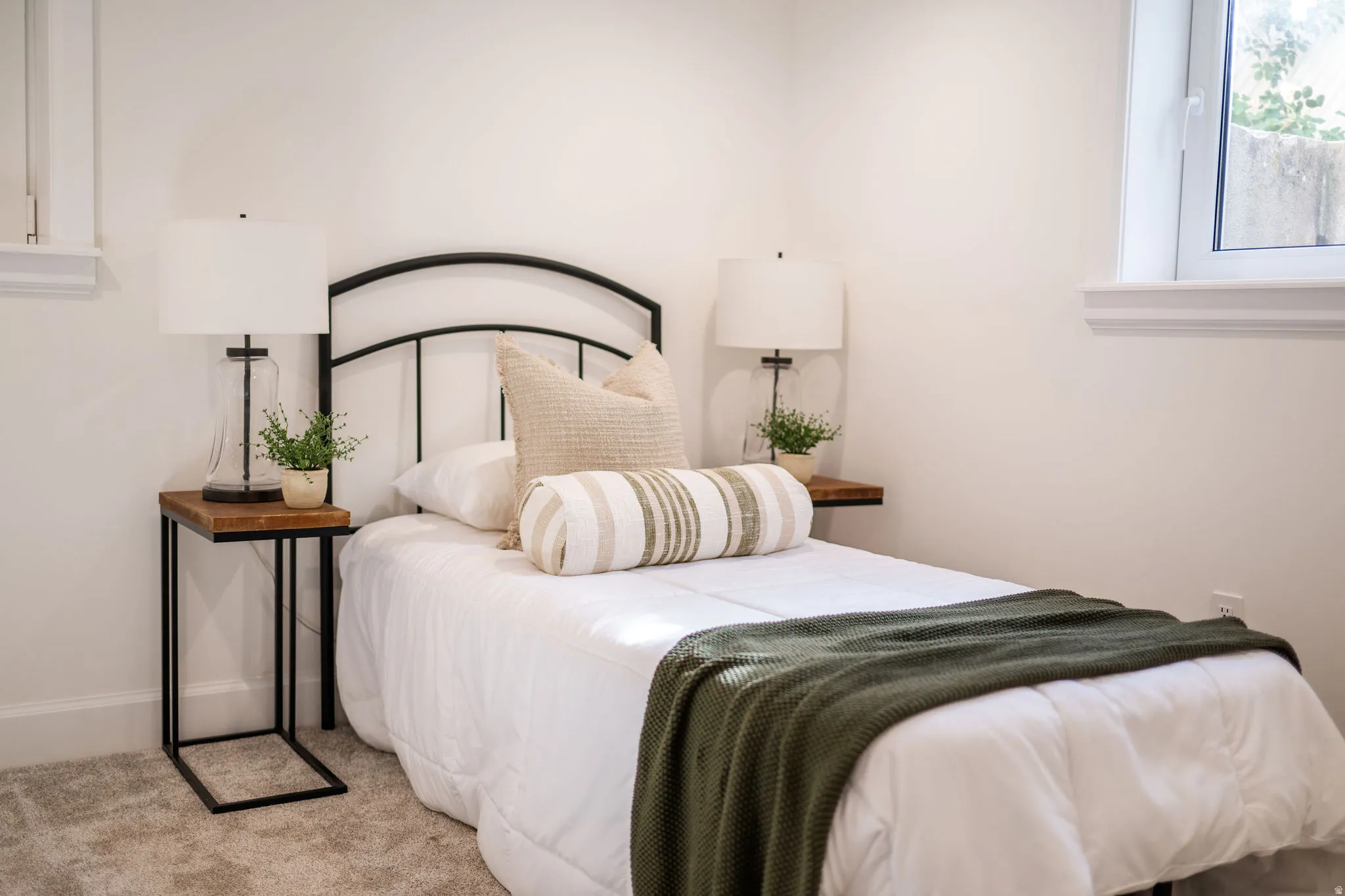 Bedroom featuring a black metal headboard, neutral-toned walls, a window with white trim, and light-colored carpet