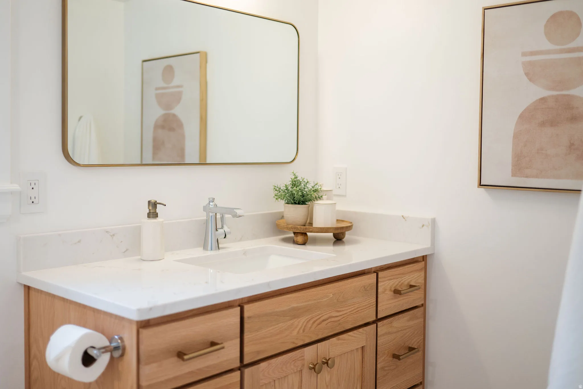 Bathroom vanity featuring a light wood-finish cabinet with brass hardware, a white countertop, an undermount sink, and a chrome faucet