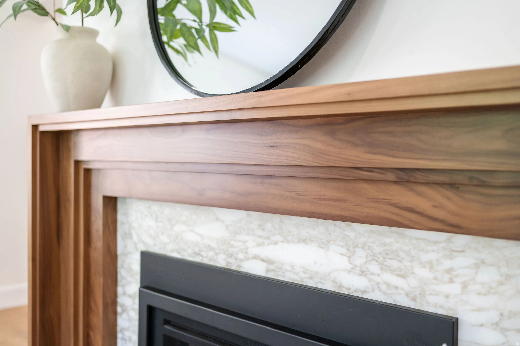 Fireplace featuring a rich walnut mantelpiece with layered detailing, a white and grey veined stone surround, and a black fireplace insert