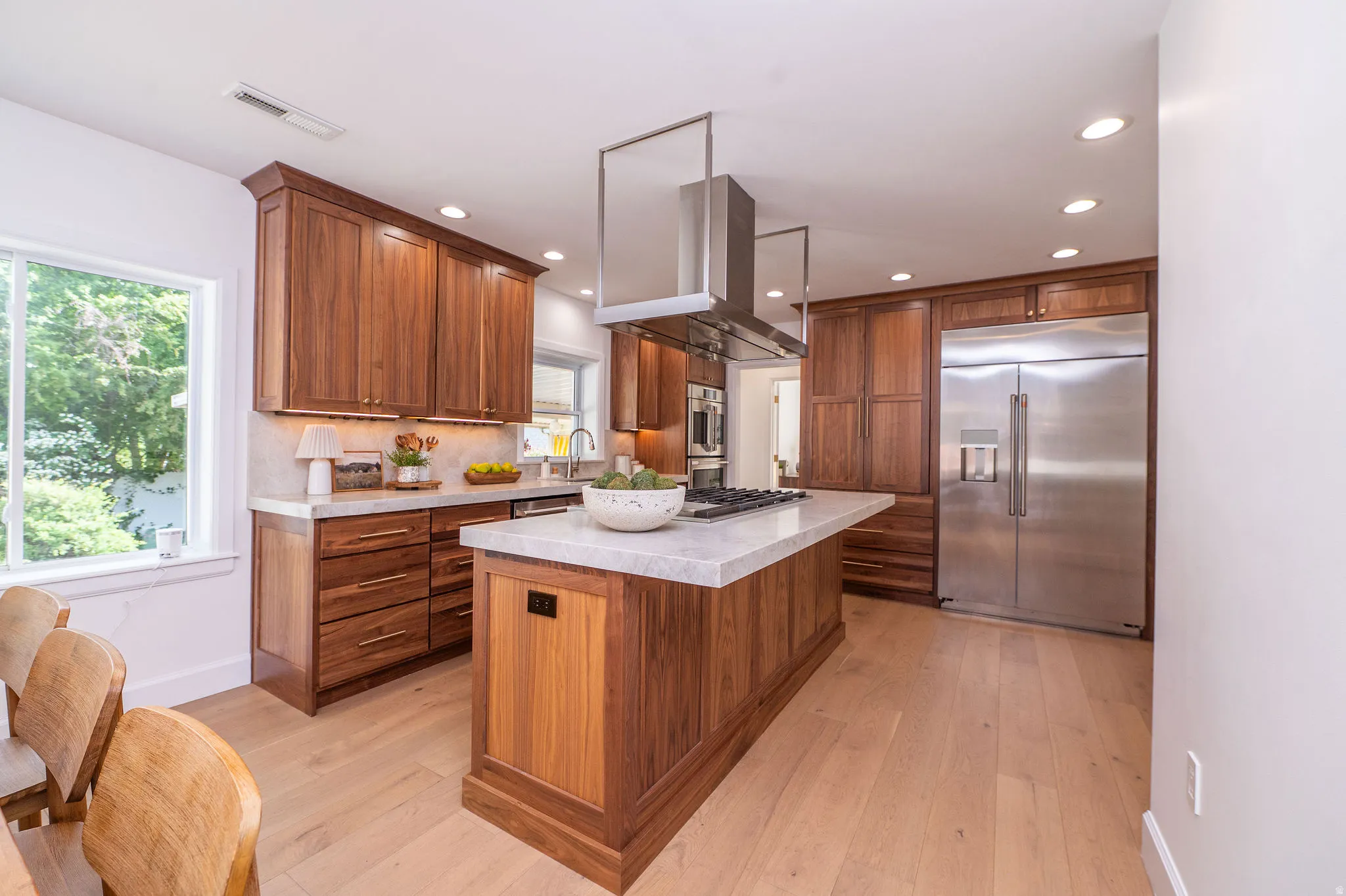 Open-concept kitchen featuring an oversized island with a gas cooktop, stainless steel range hood, ample cabinetry, wood-finish flooring, and recessed lighting