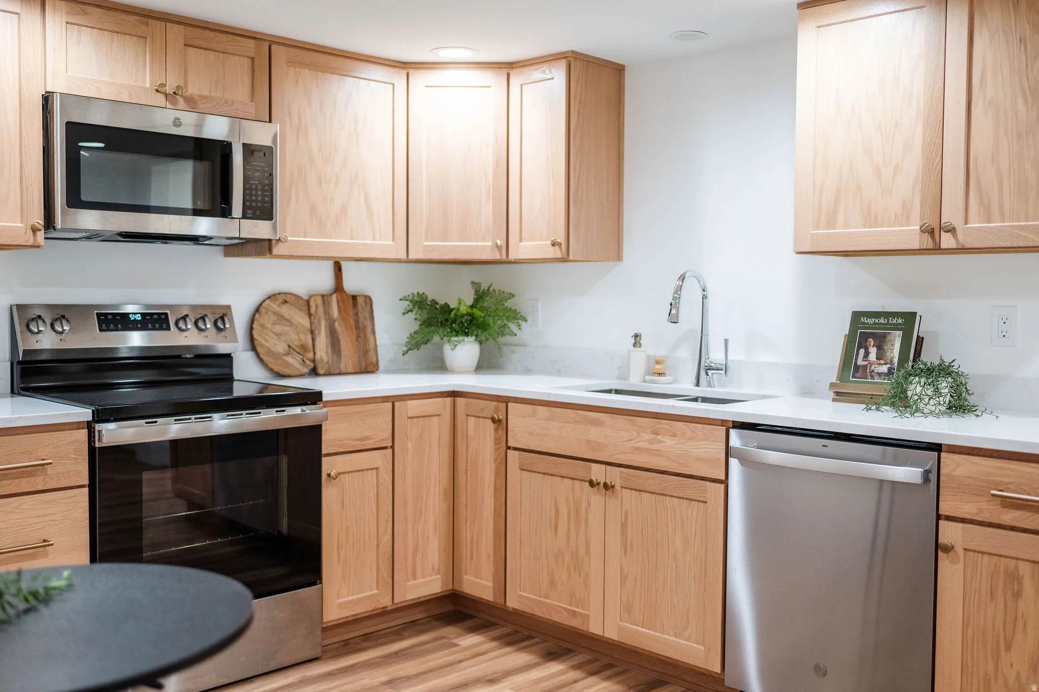 Kitchen featuring natural wood-finish cabinetry, stainless steel appliances, white countertops, and a stainless steel sink with a gooseneck faucet