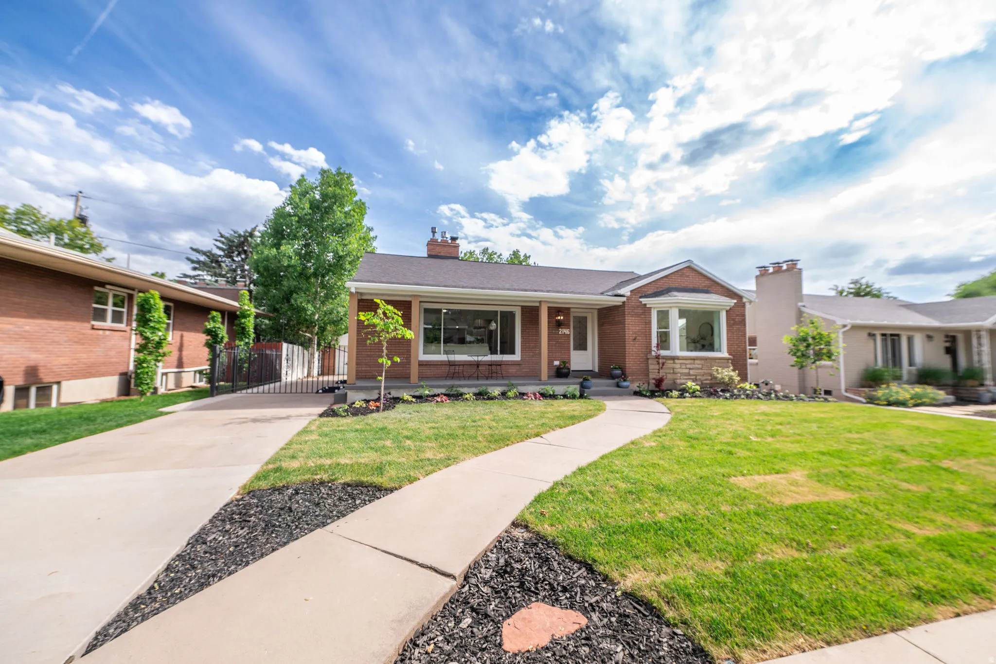 Brick-clad residence featuring a bay window, a covered front porch, and a concrete pathway leading to the entrance