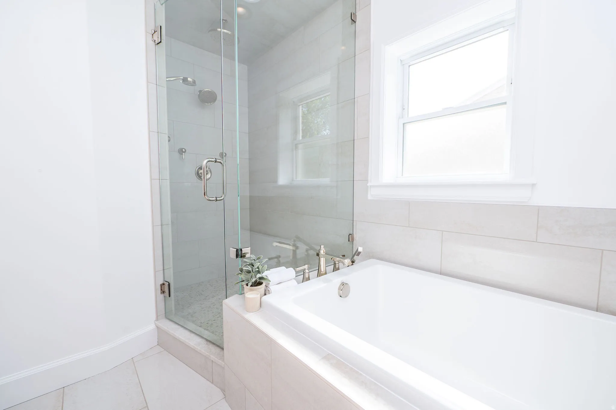 Contemporary bathroom featuring a frameless glass shower enclosure, a built-in soaking tub, a window with white trim, and light-toned tile flooring