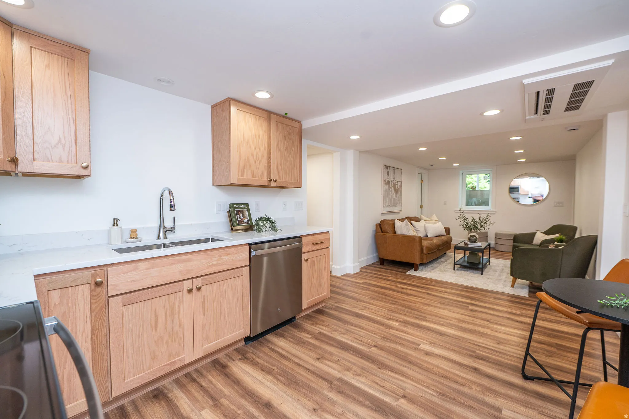 Open-concept living area featuring wood-finish flooring, recessed lighting, and a kitchen with light wood cabinetry, white countertops, and stainless steel appliances