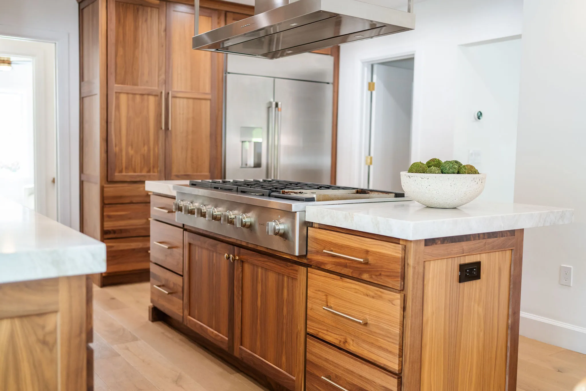 Gourmet kitchen island featuring a stainless steel gas range with a matching overhead vent hood, ample wood cabinetry, light-toned countertops, and wood-finish flooring