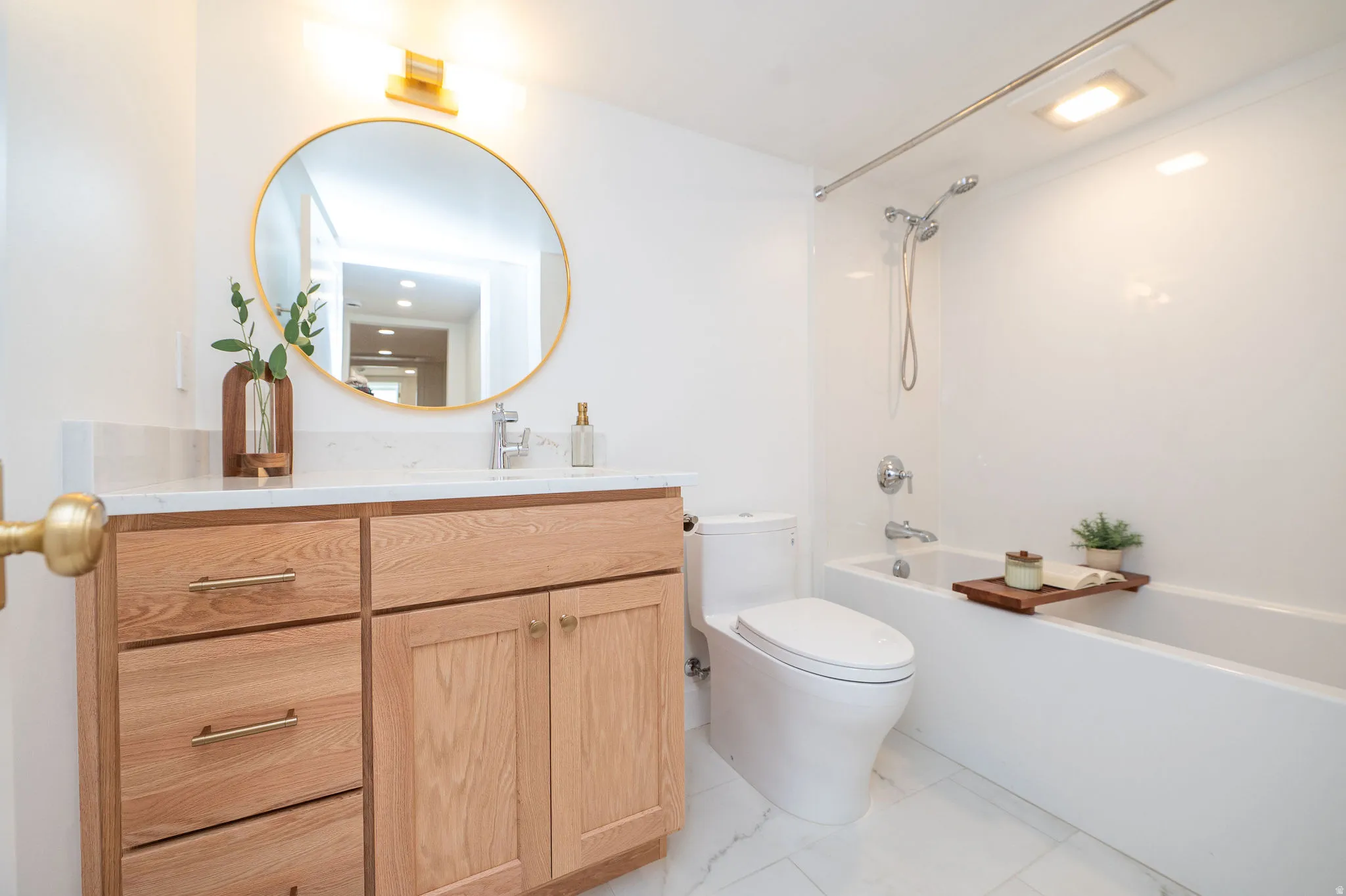 Bathroom featuring a wood-finish vanity with a light-colored countertop, a circular gold-framed mirror, and a full bathtub with a shower fixture