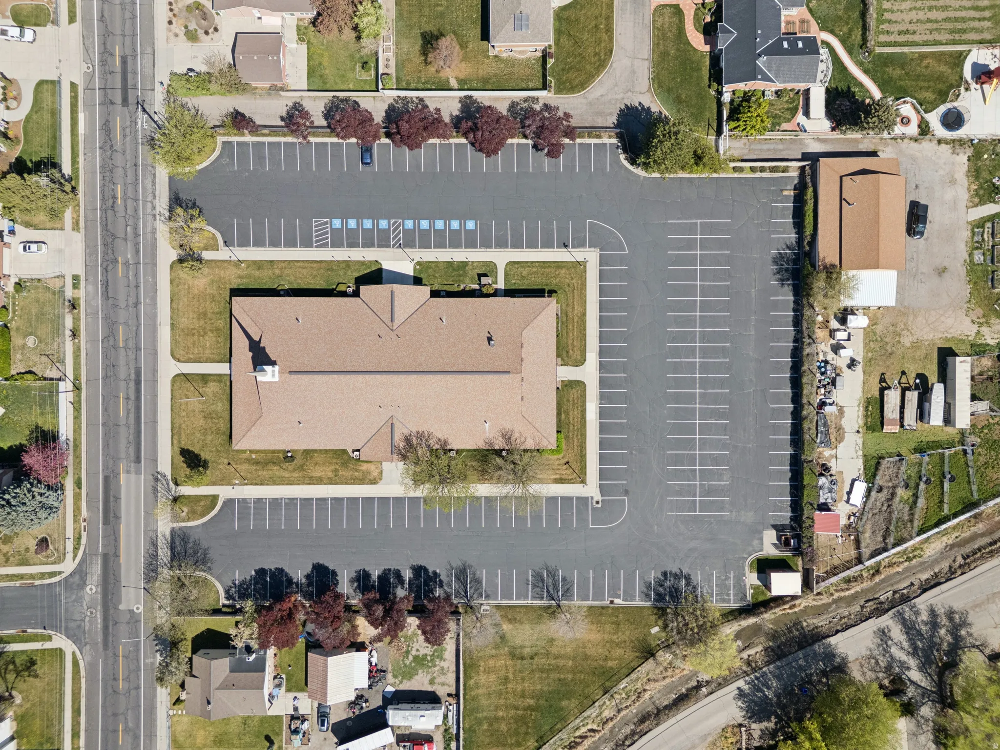 Spacious property featuring a large structure with a brown shingled roof, extensive paved parking areas, and surrounding green lawn.