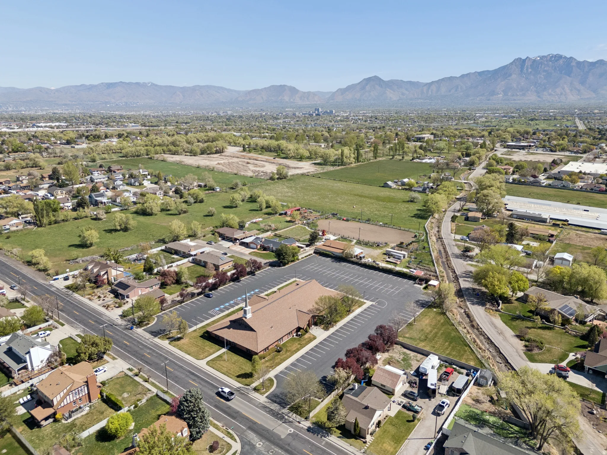 Expansive aerial perspective showcasing a neighborhood with residential properties, green spaces, and a commercial building featuring a large parking area