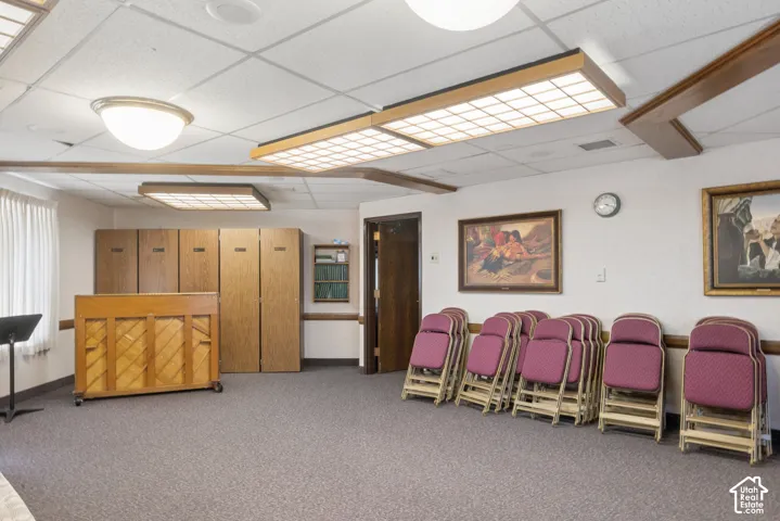 Spacious room featuring neutral carpet flooring, recessed ceiling lighting, and a white acoustical tile ceiling.