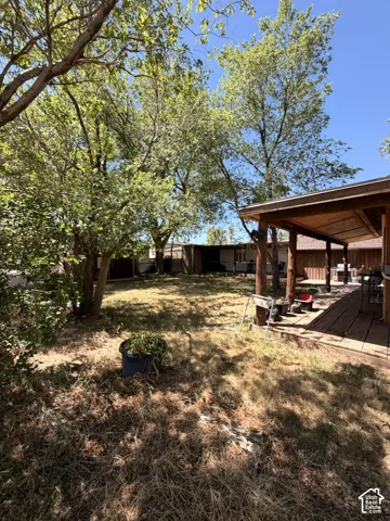 Expansive outdoor space featuring a covered wood deck, mature trees, and a wooden privacy fence