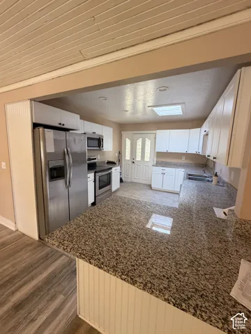 Kitchen featuring granite countertops, white cabinetry, stainless steel appliances, recessed lighting, and wood-finish flooring