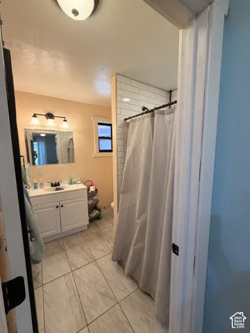 Bathroom featuring a white vanity with integrated sink, a three-light fixture, and subway tile shower surround
