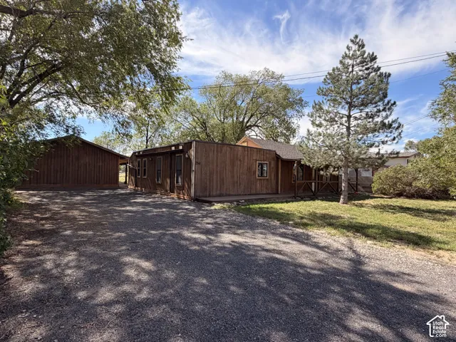 Wood-sided exterior with covered porch, gravel driveway, and mature landscaping