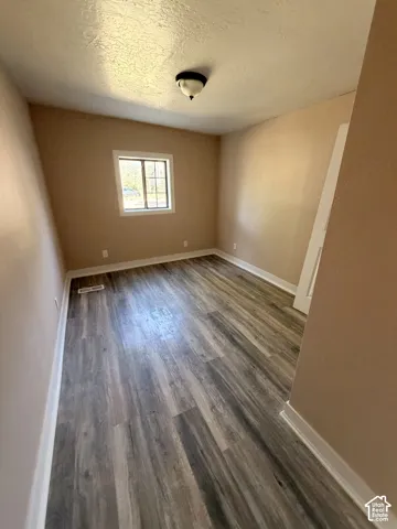 Bright, spacious bedroom with wood-finish plank flooring, neutral wall tones, and abundant natural light from a large window