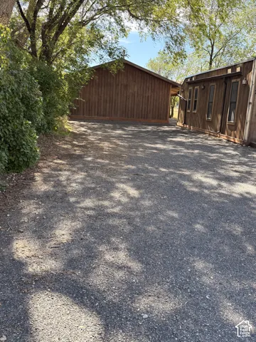Gravel surface entryway bordered by mature trees and established shrubs