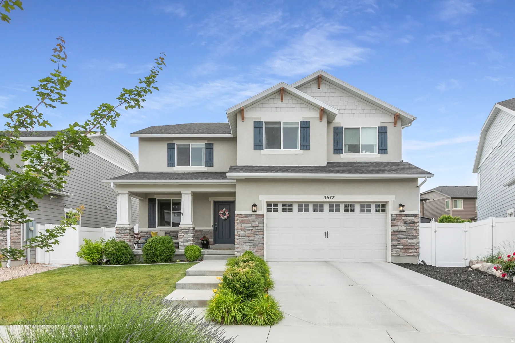 Two-story exterior featuring a stone and stucco finish, a covered front porch with columns, a two-car garage, and a concrete driveway