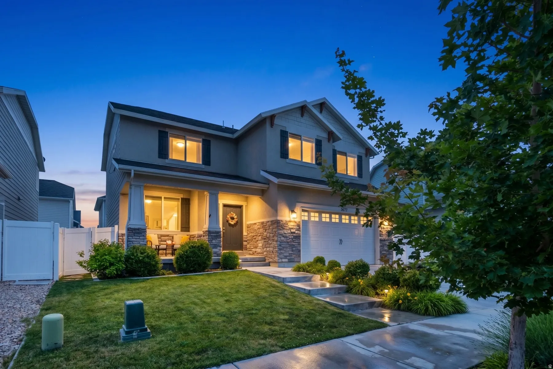 Two-story residence featuring a covered front porch with pillar supports, a two-car garage, stone and siding exterior, and a manicured lawn with established landscaping