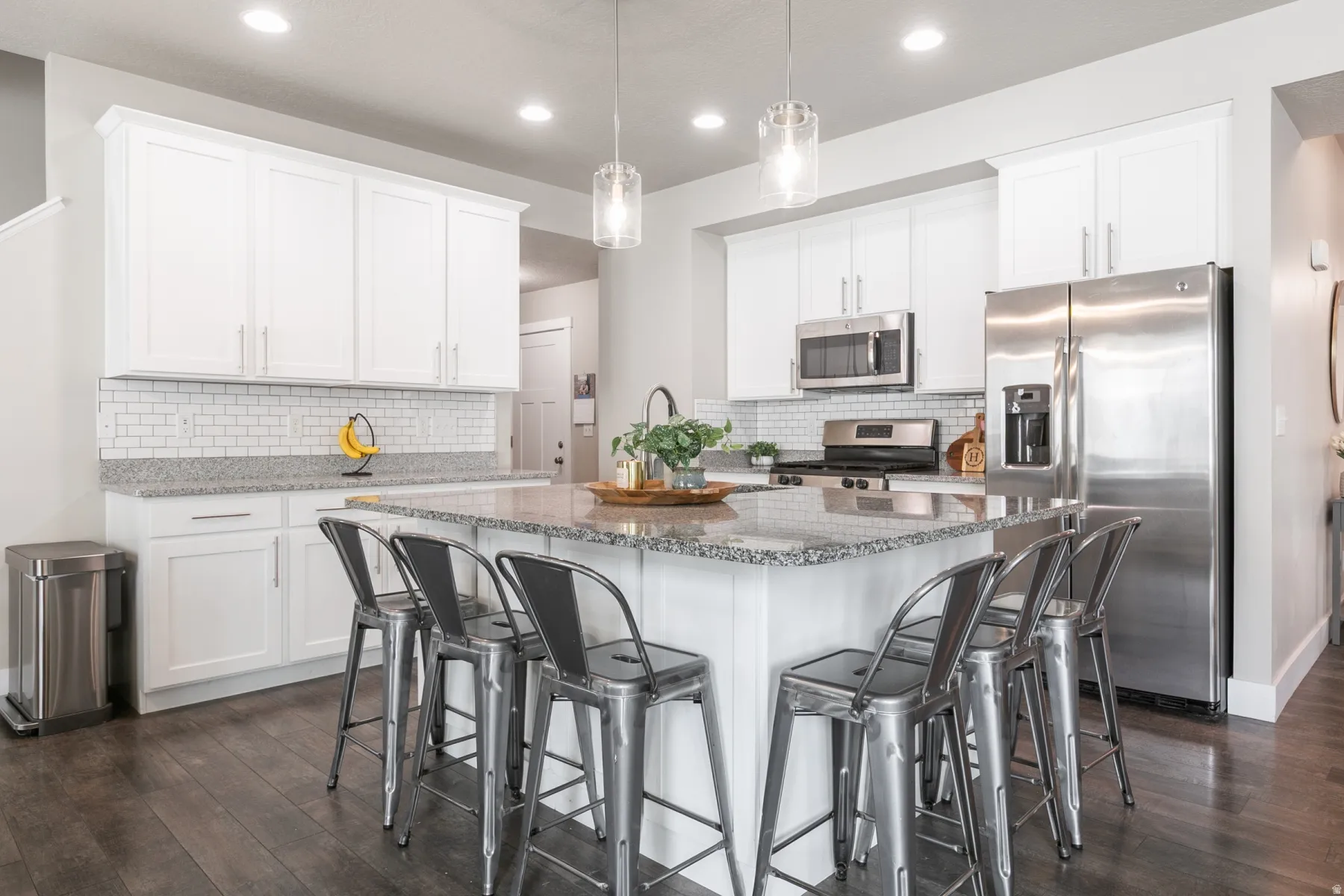 Kitchen featuring a large island with granite countertop, white shaker cabinetry, subway tile backsplash, stainless steel appliances, and dark wood-finish flooring