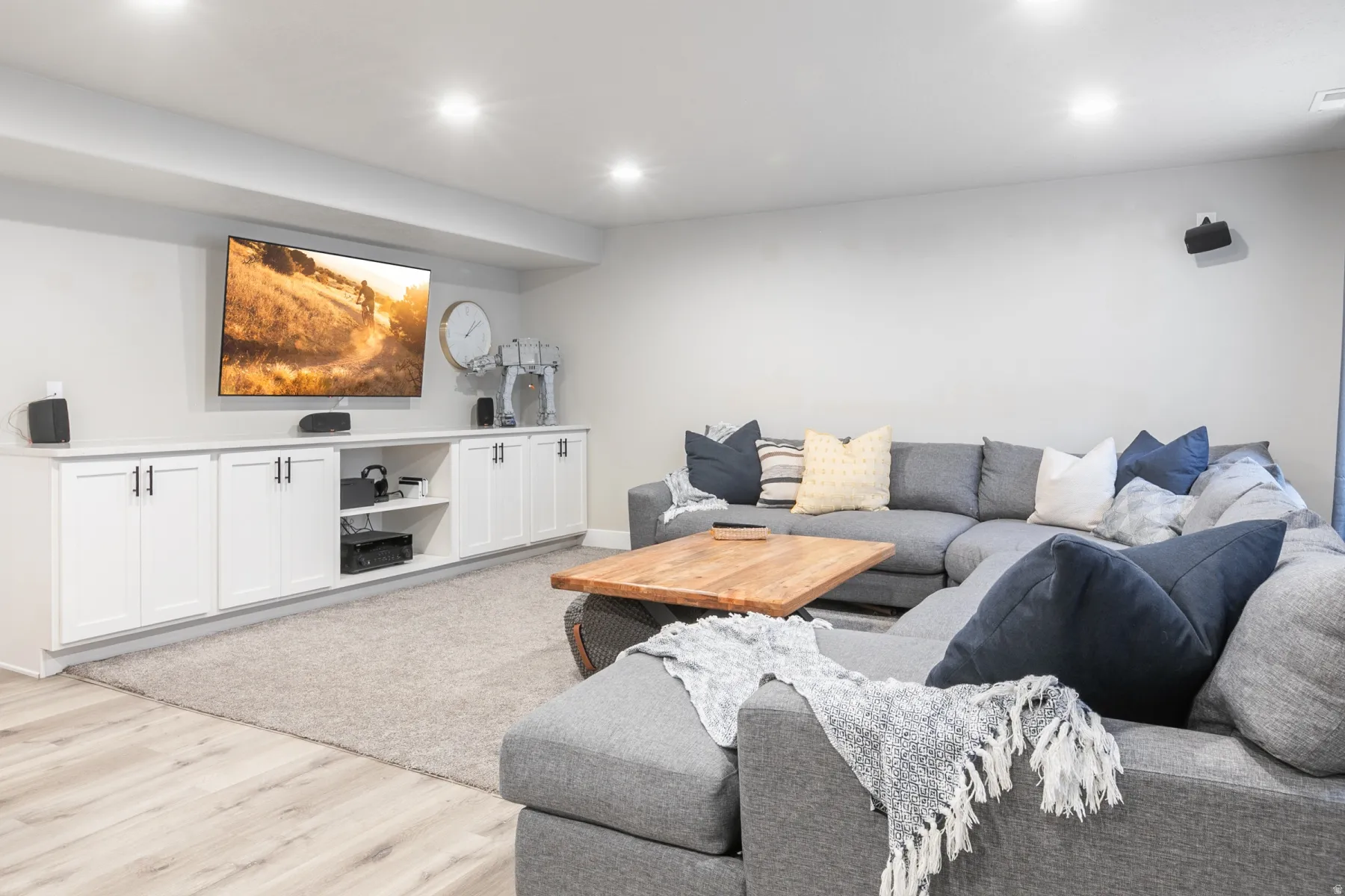 Spacious entertainment area featuring recessed lighting, a built-in media console with white cabinetry and dark hardware, and light wood-finish flooring