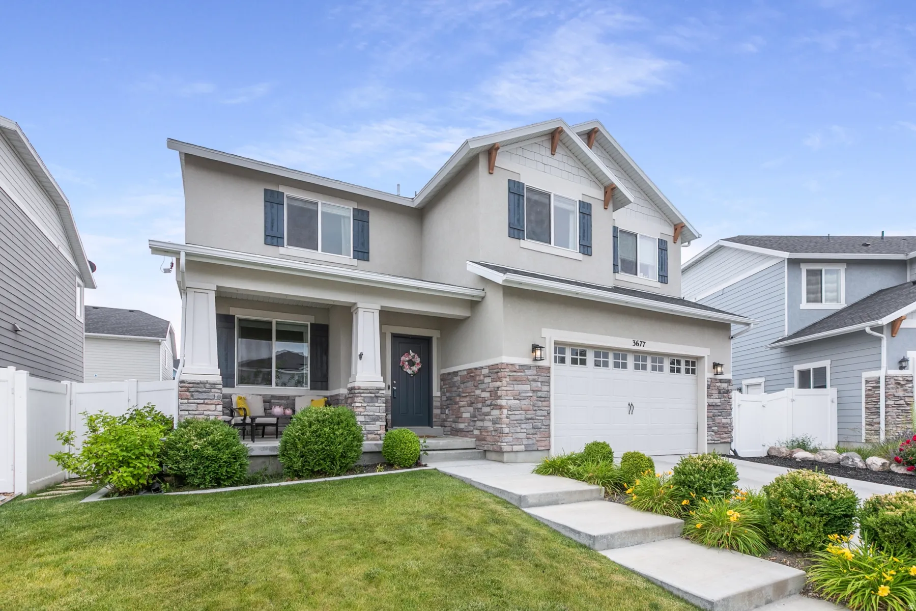Contemporary two-story residence featuring a covered front porch, stone veneer accents, a dedicated garage, and mature landscaping