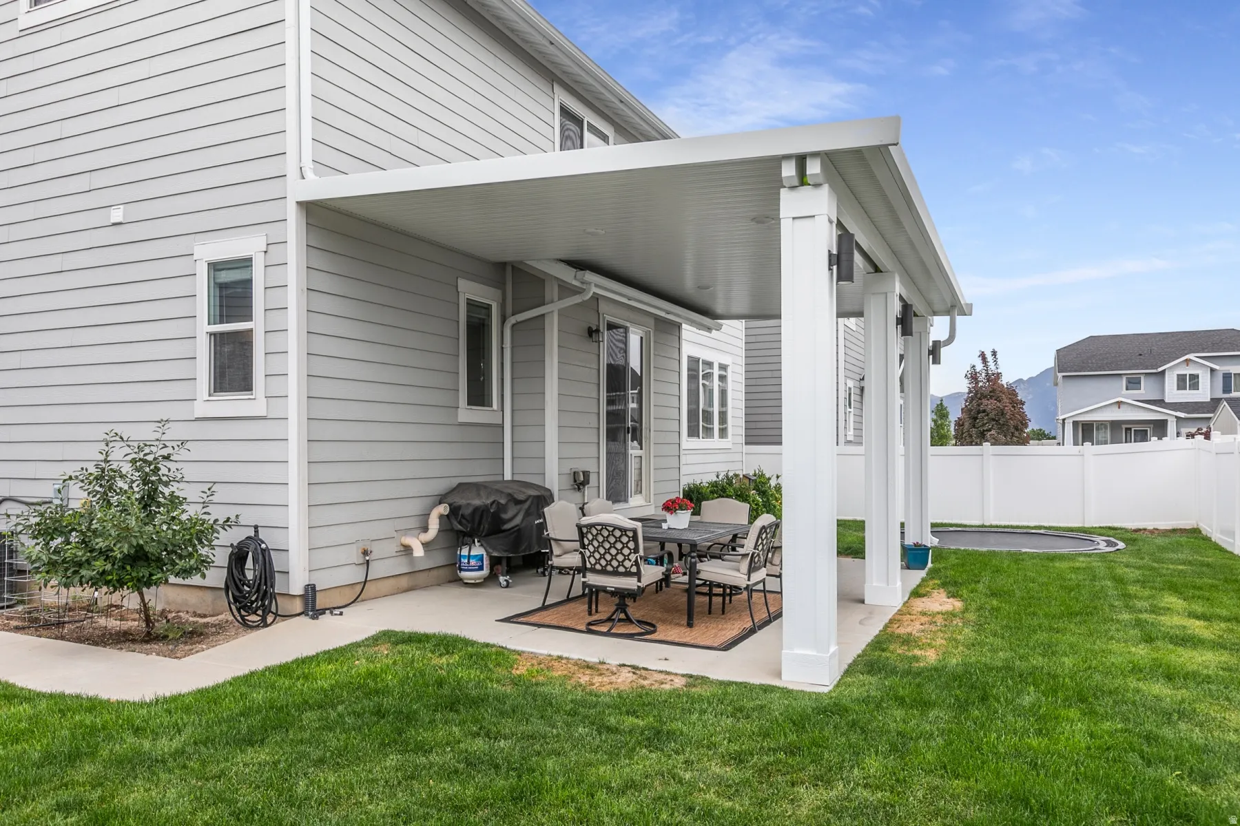 Spacious rear yard featuring a covered patio, concrete slab, manicured lawn, and white privacy fencing