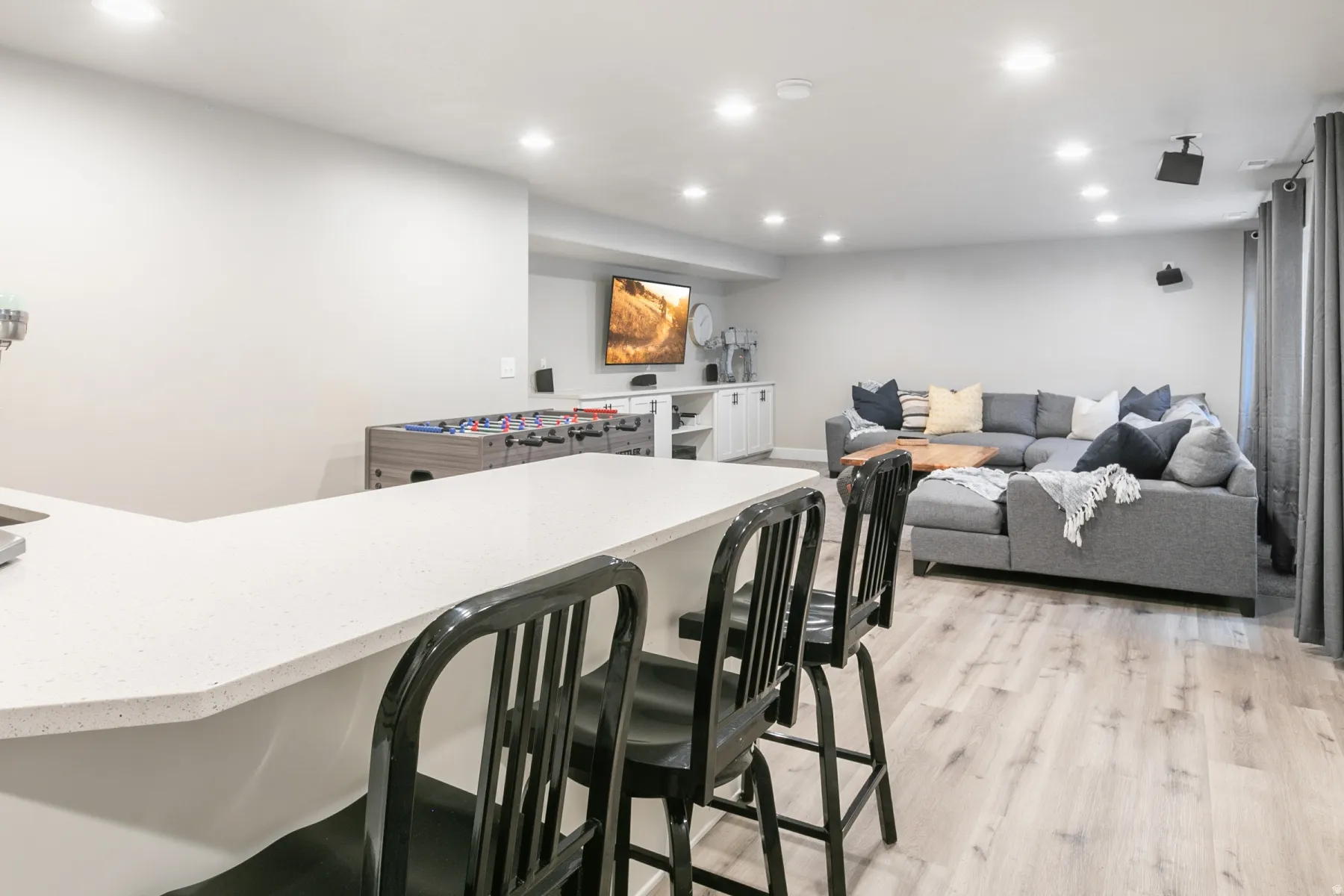 Spacious entertainment area featuring a white countertop bar, light wood-finish flooring, recessed lighting, built-in cabinetry, and a wall-mounted television