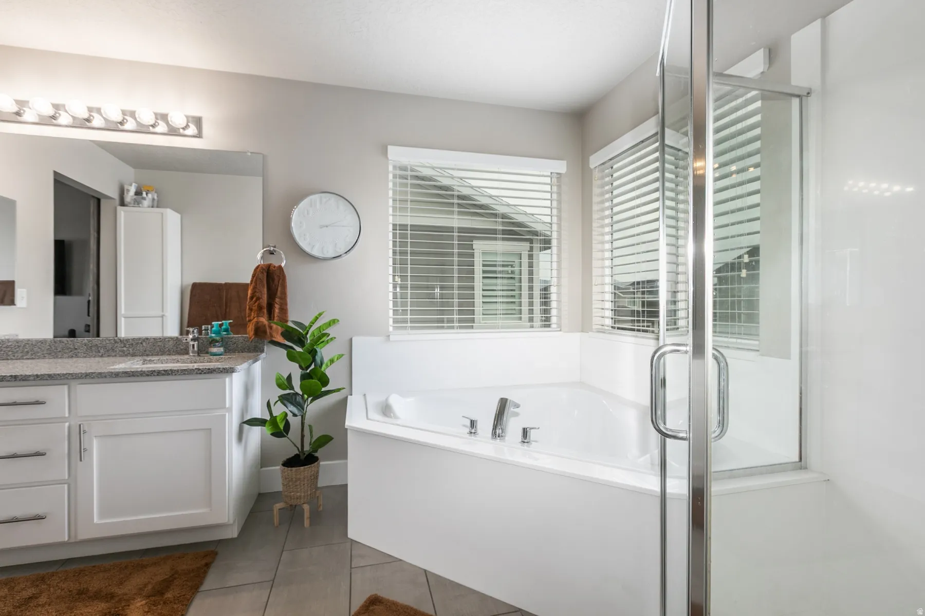 Corner soaking tub with a glass-enclosed shower, dual-sink vanity with a granite-style countertop, and white cabinetry