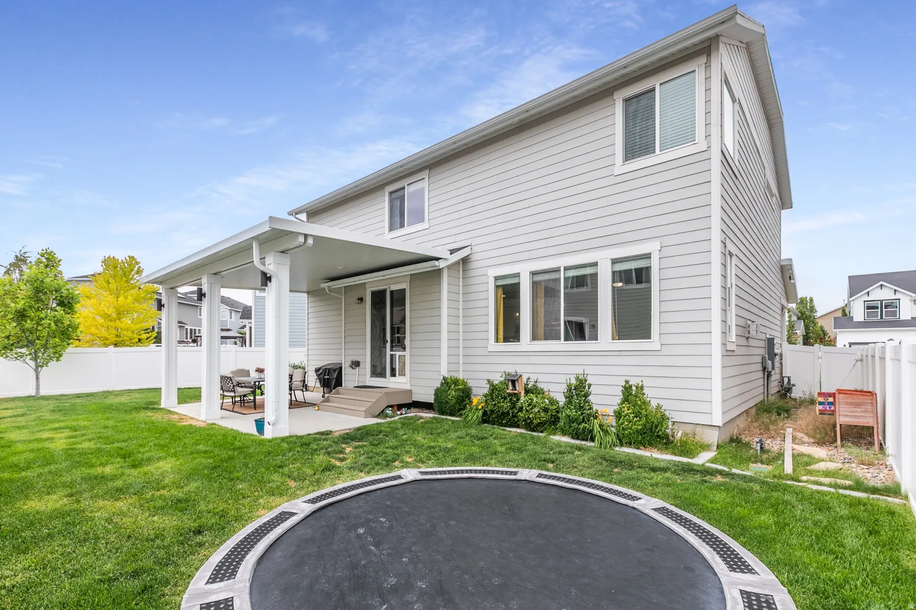 Rear exterior featuring light grey siding, multiple windows, and a covered patio with concrete flooring