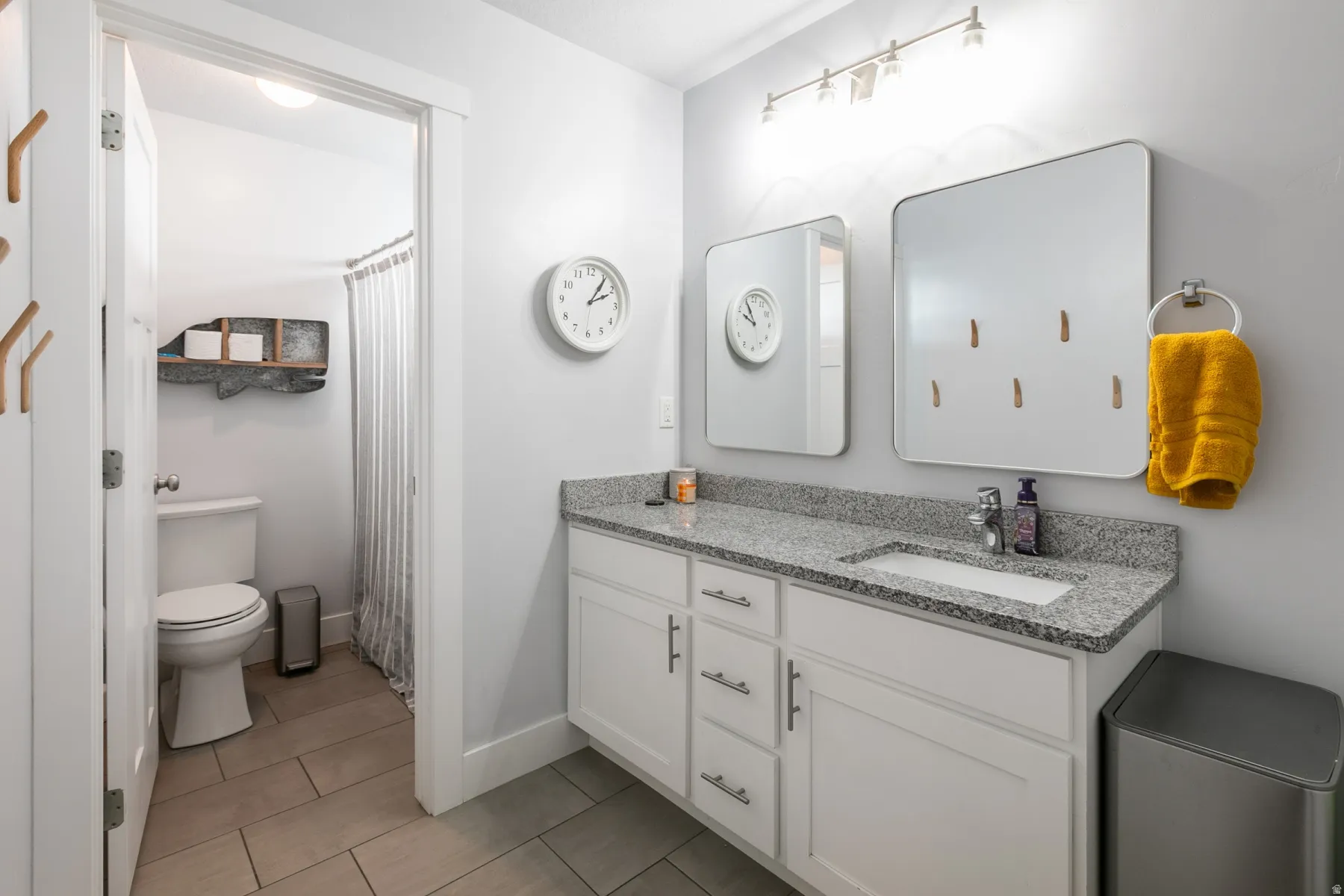 Contemporary bathroom featuring a vanity with granite-look countertop and dual mirrors, complemented by a white toilet and a shower area