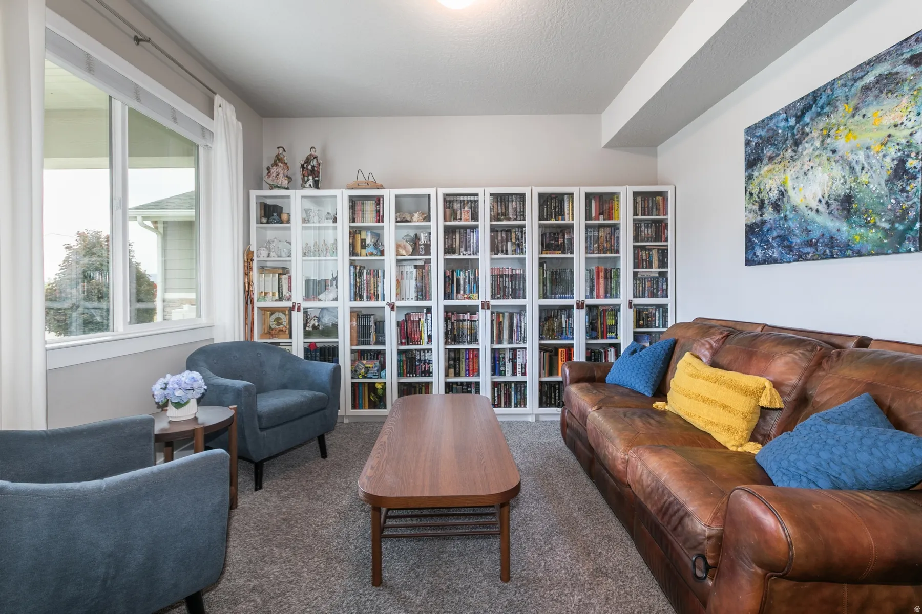 Living area featuring a wall of built-in shelving, neutral carpeting, and a large window