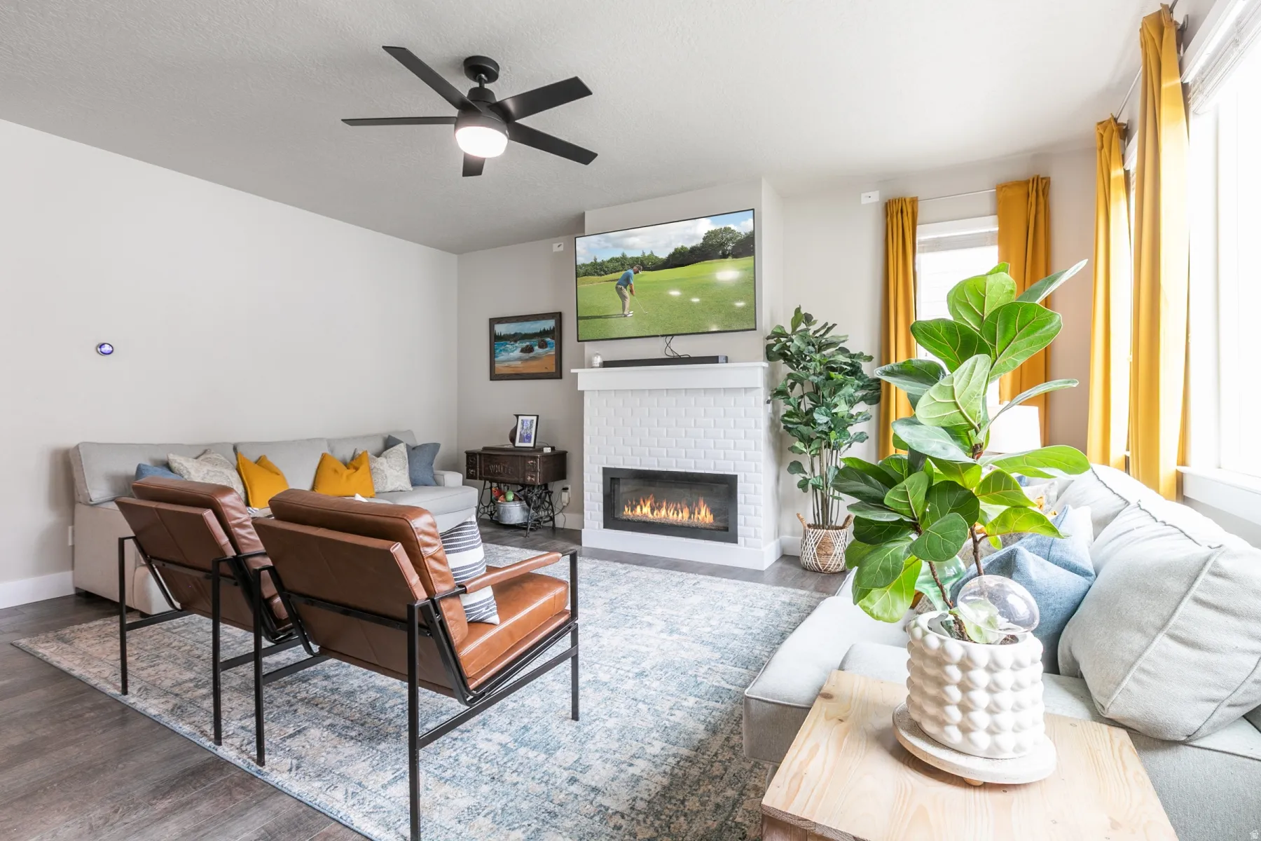 Living area featuring a white brick fireplace with a visible flame insert, wood-finish flooring, and a ceiling fan with integrated lighting