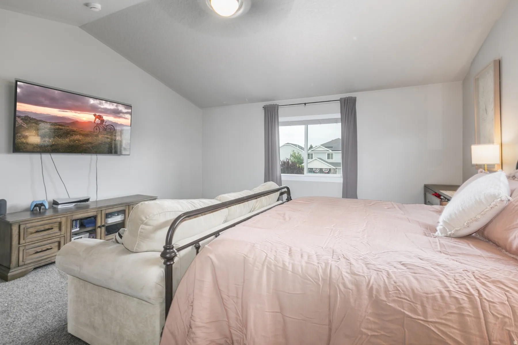 Carpeted bedroom featuring vaulted ceilings, a wall-mounted television, and a window with curtains