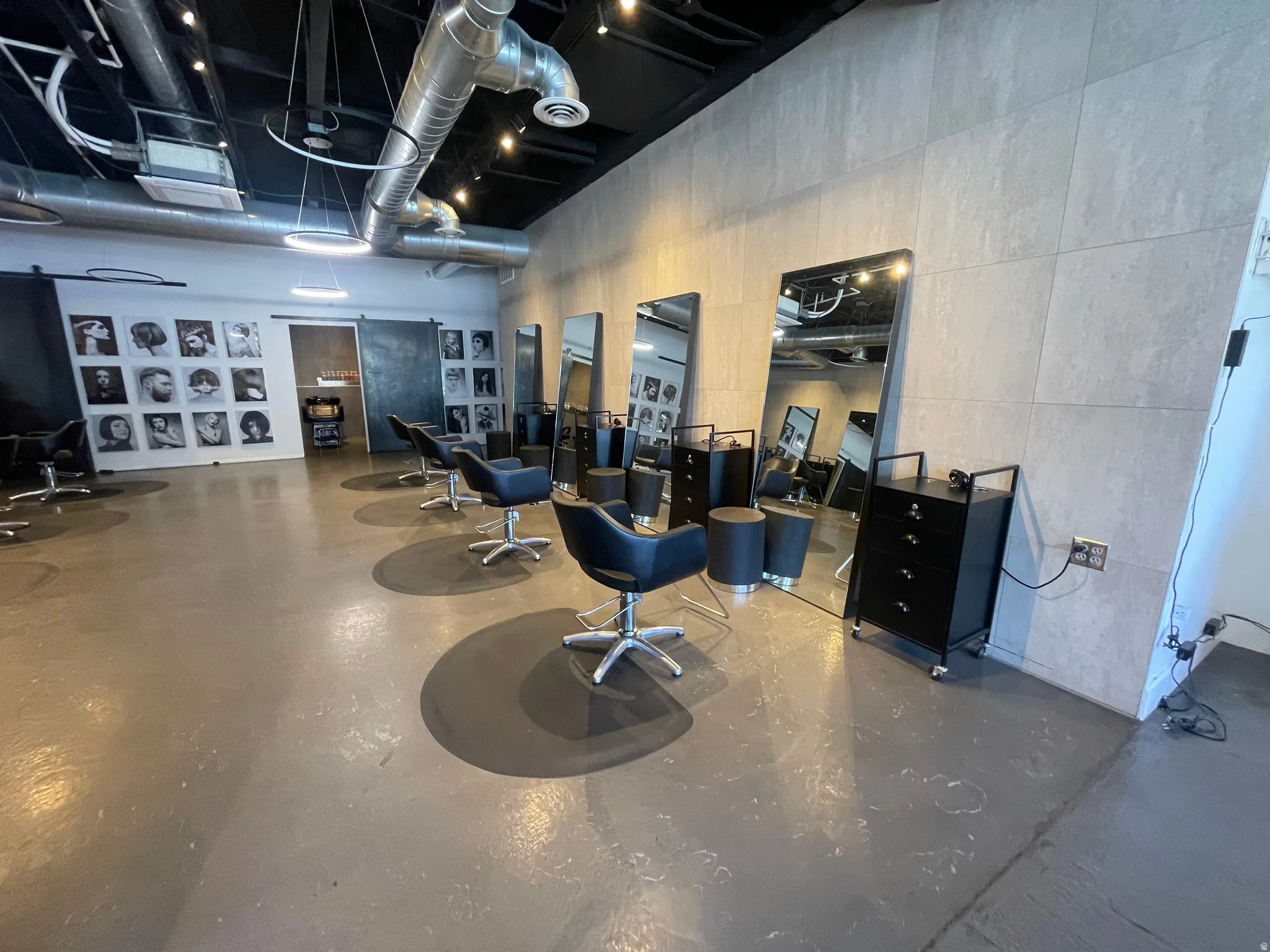 Commercial interior featuring multiple styling stations, concrete-finish flooring, exposed ductwork, track lighting, and a barn door entry