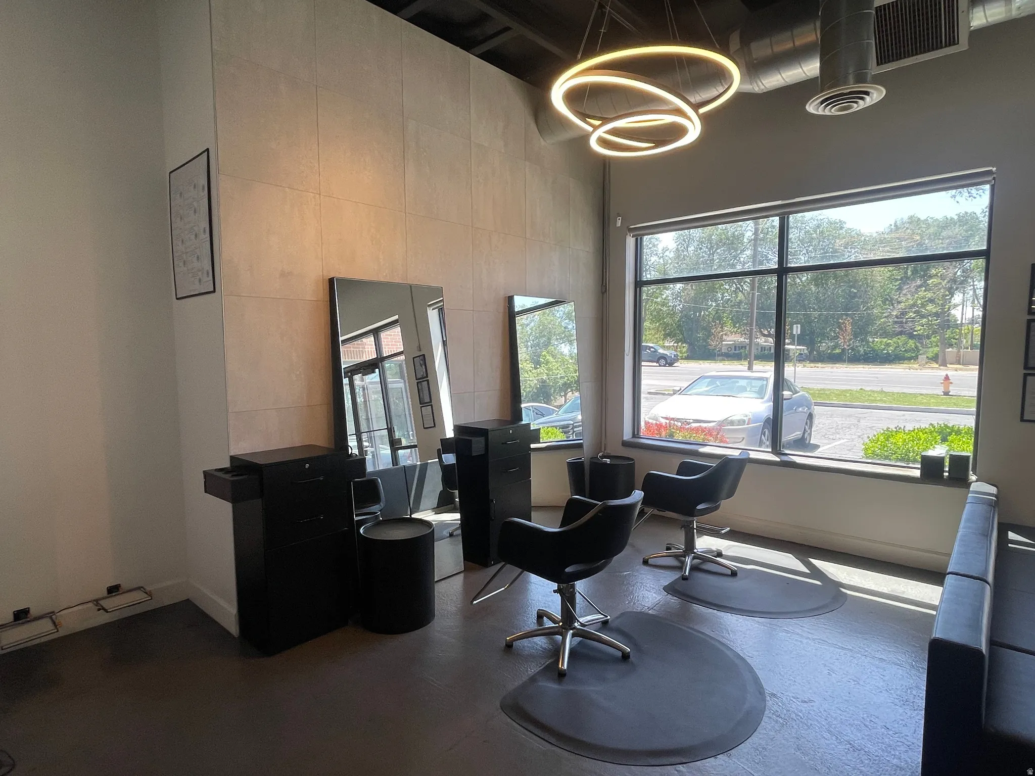 Contemporary commercial interior featuring a full-height window, exposed ductwork, large format wall tiling, and modern circular pendant lighting