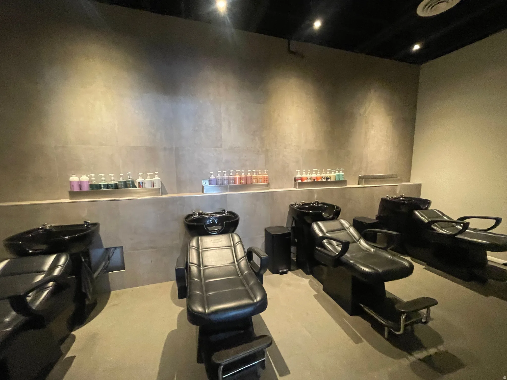 Treatment area featuring multiple black salon chairs and integrated wash basins