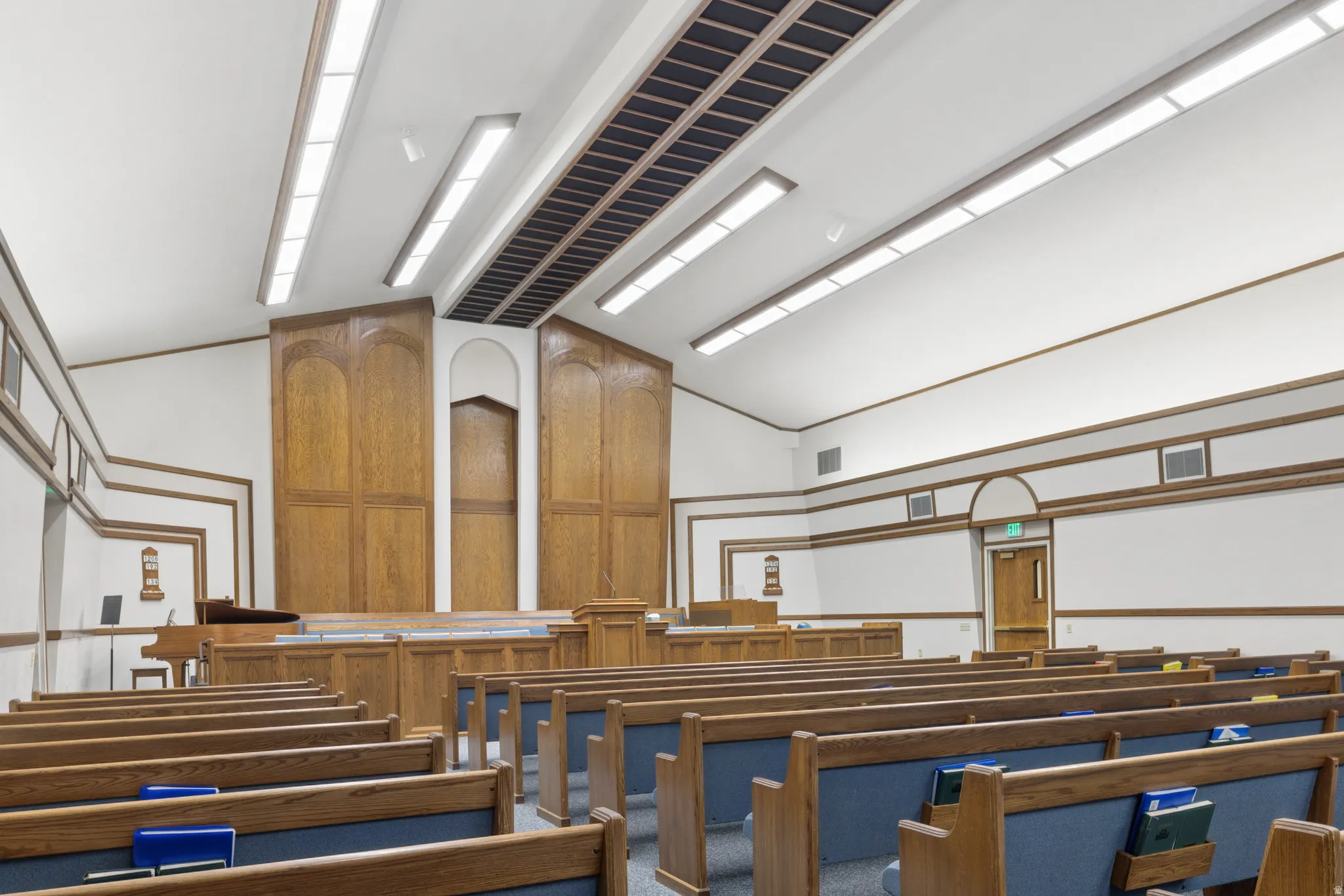 Spacious assembly room featuring extensive rows of wooden pews with blue upholstered seating.