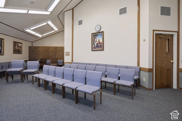 Spacious interior featuring a vaulted ceiling with integrated fluorescent lighting panels, textured wall-to-wall carpeting, wood-paneled accents, and a solid wood entry door with a window.