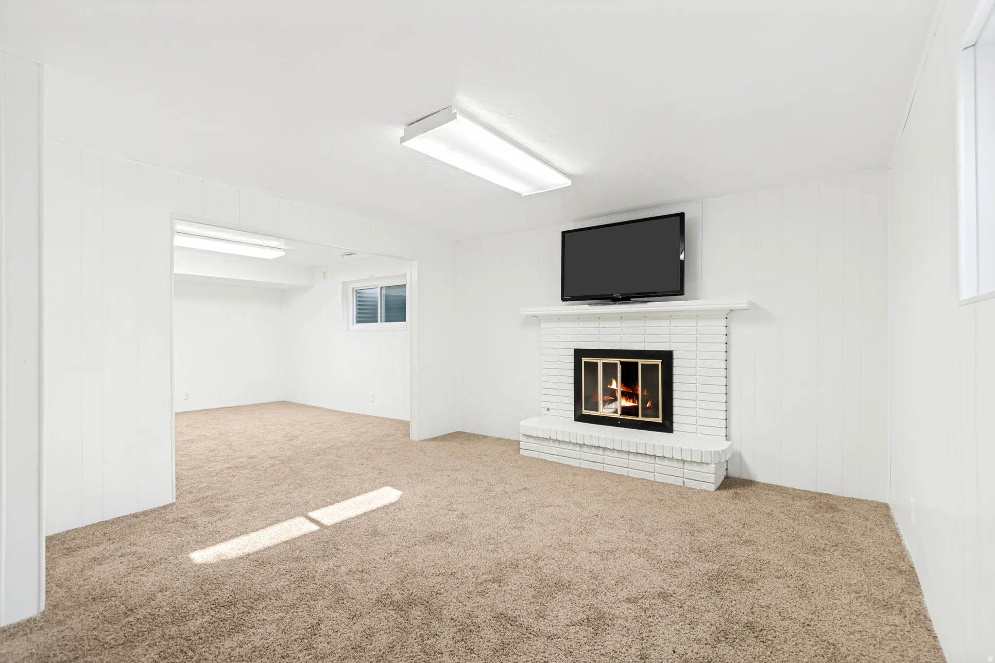 Spacious room featuring a white brick fireplace with a hearth, light brown carpet, and white paneling on the walls