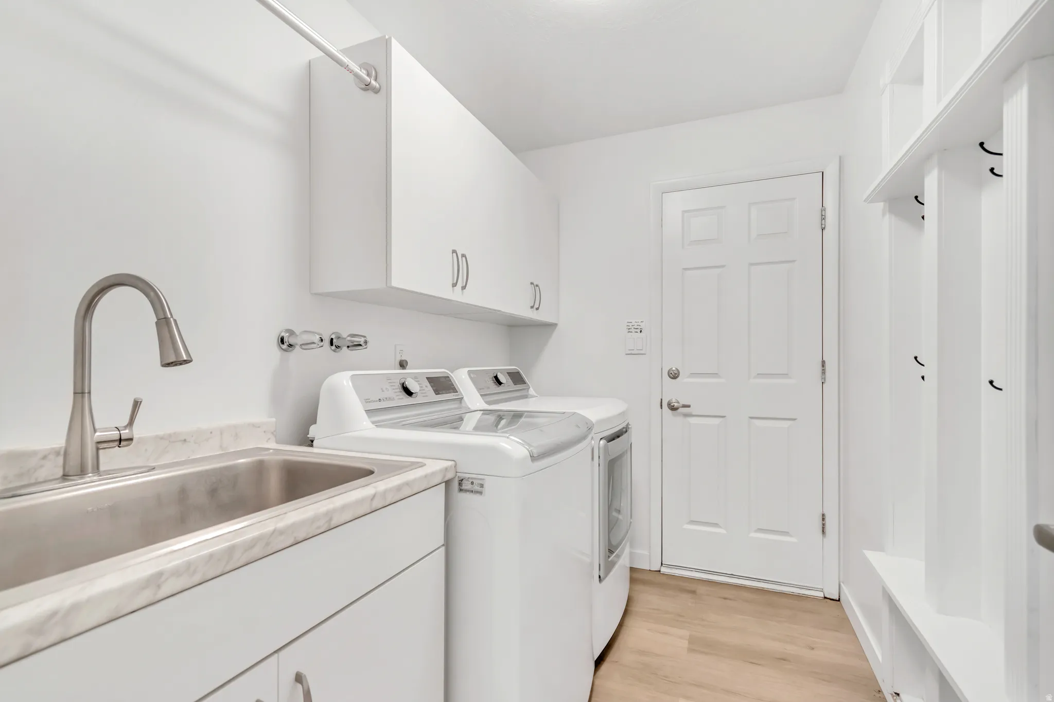 Utility room featuring a stainless steel sink, solid surface countertop, white cabinetry, and wood-finish flooring
