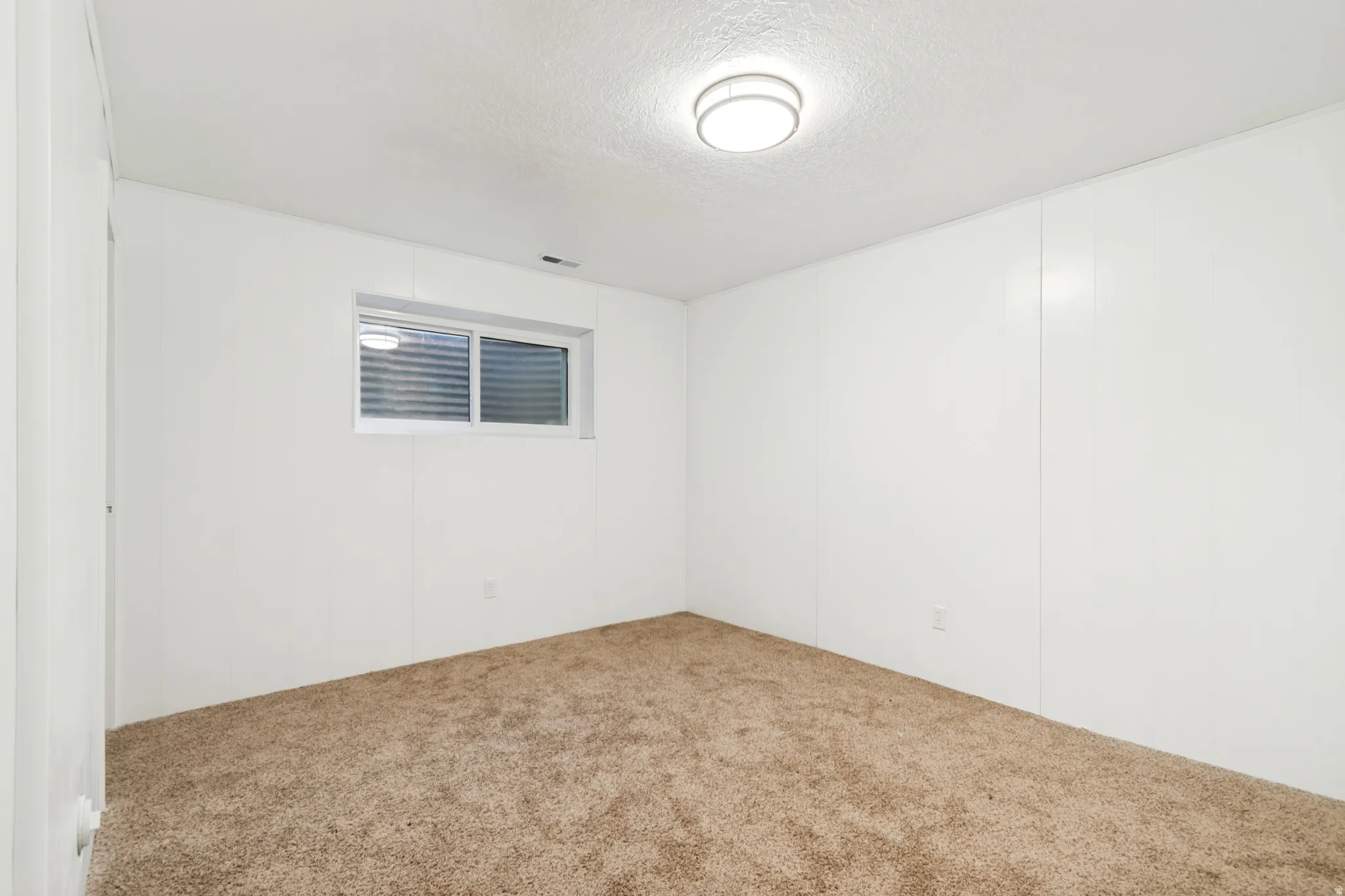 Room featuring white paneling, brown carpet flooring, and a single window with horizontal blinds