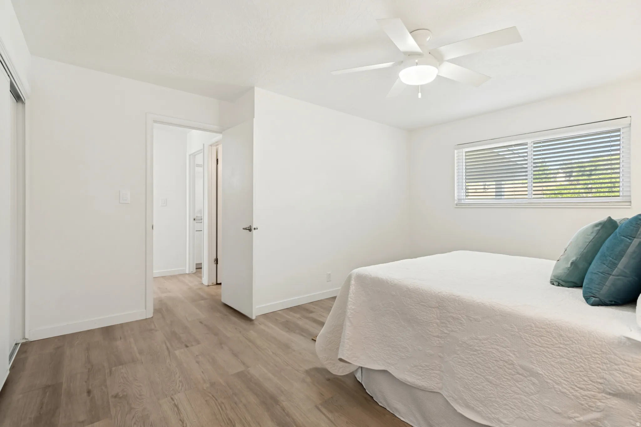 Interior room with wood-finish flooring, white walls, and a white ceiling fan with integrated lighting