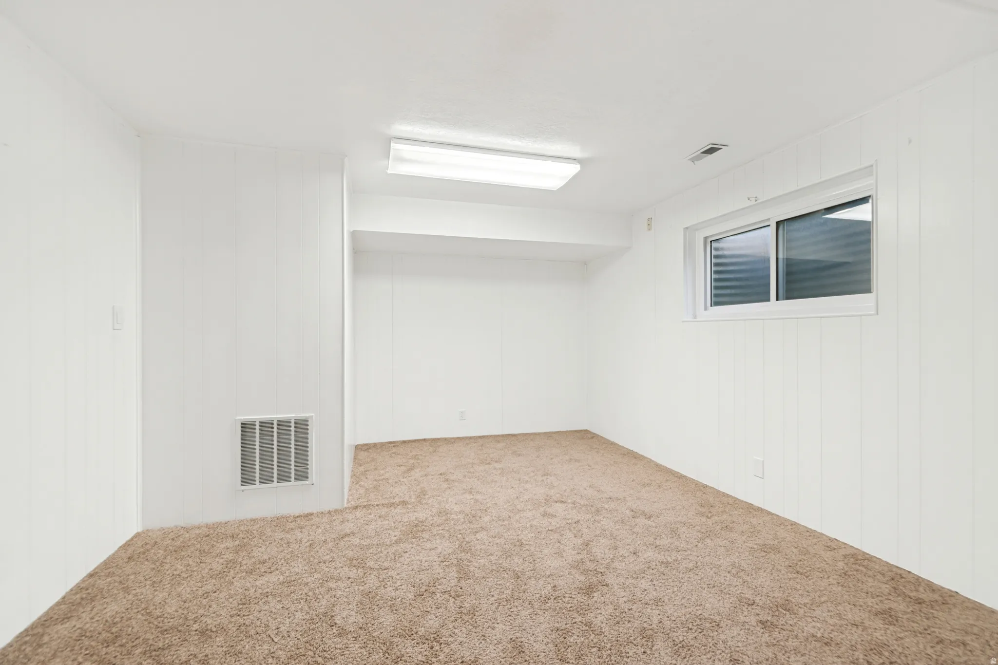 Carpeted room featuring white vertical paneling and a horizontal sliding window