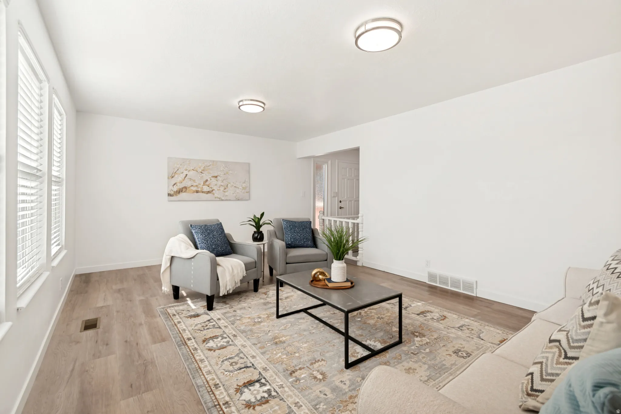 Bright living space featuring wood-finish flooring, white walls, and a pair of windows with white louvered blinds