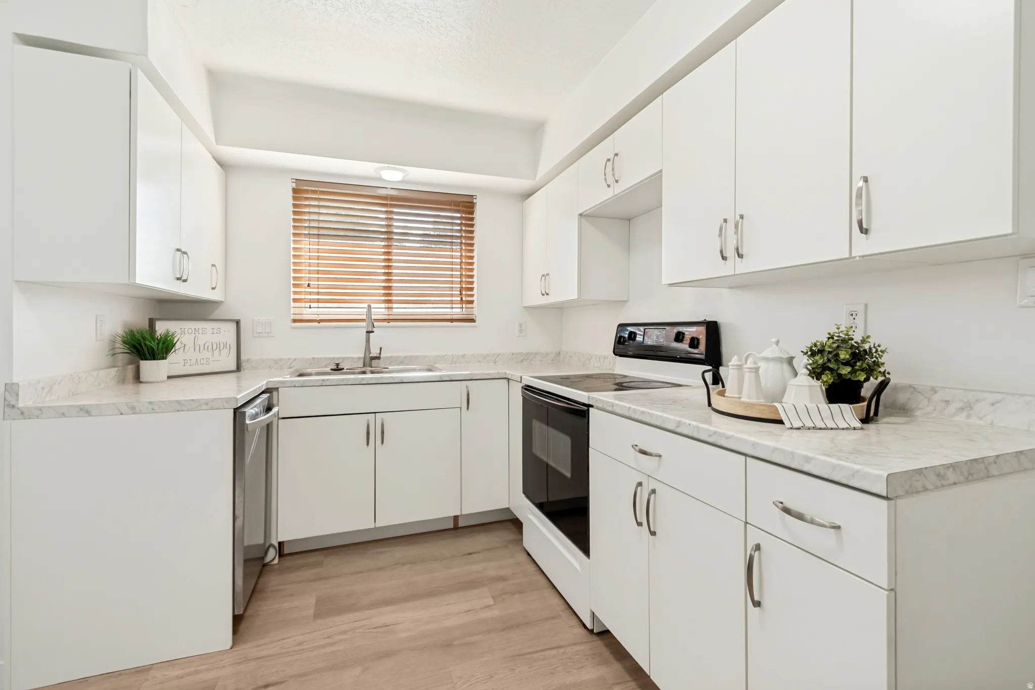 Kitchen featuring white cabinetry with silver-tone hardware, a stainless steel sink with a gooseneck faucet, light-toned countertops with subtle marbling, and wood-finish flooring