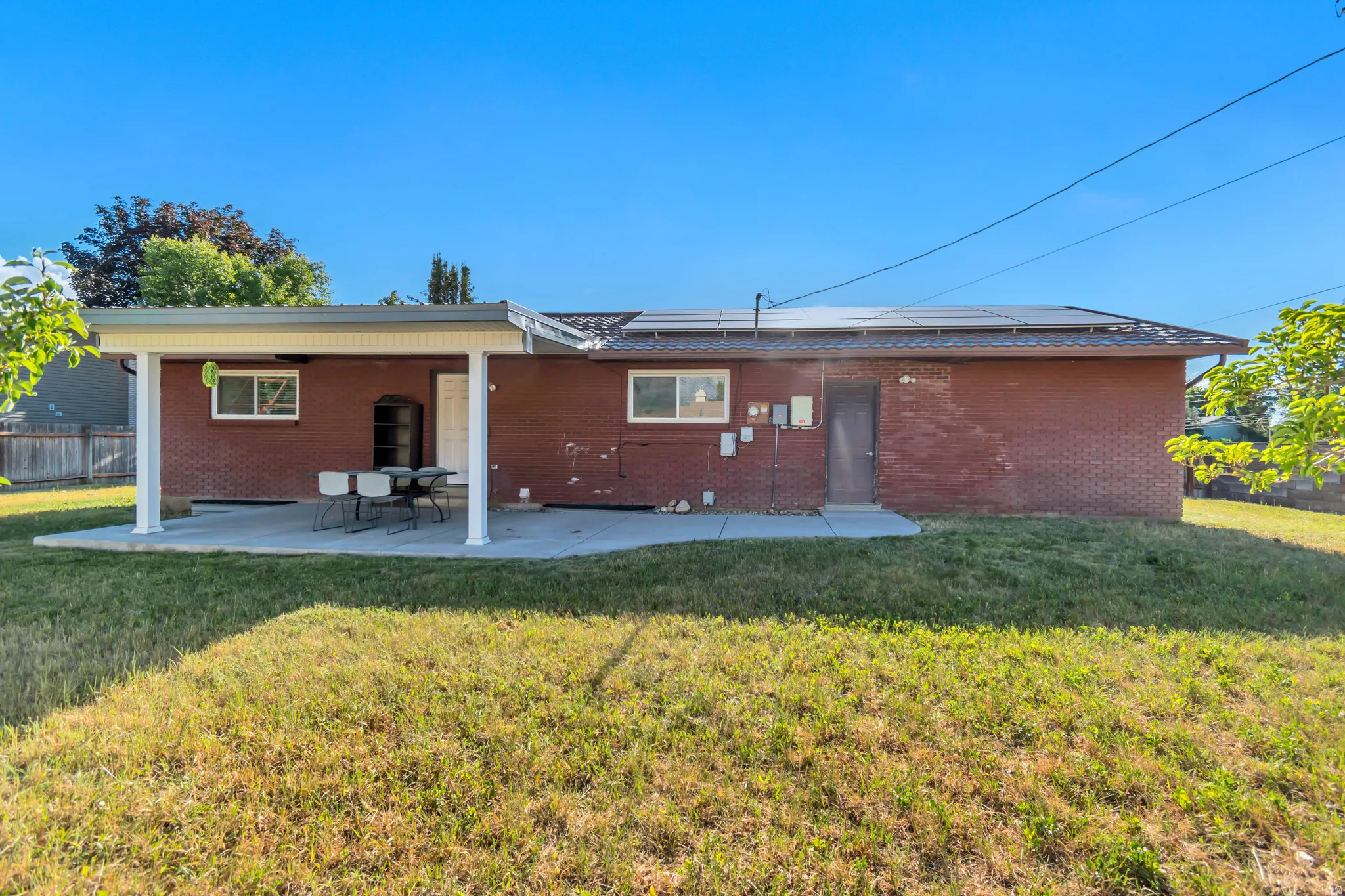 Rear exterior featuring a covered patio, red brick facade, multiple solar panels, and a concrete patio surface